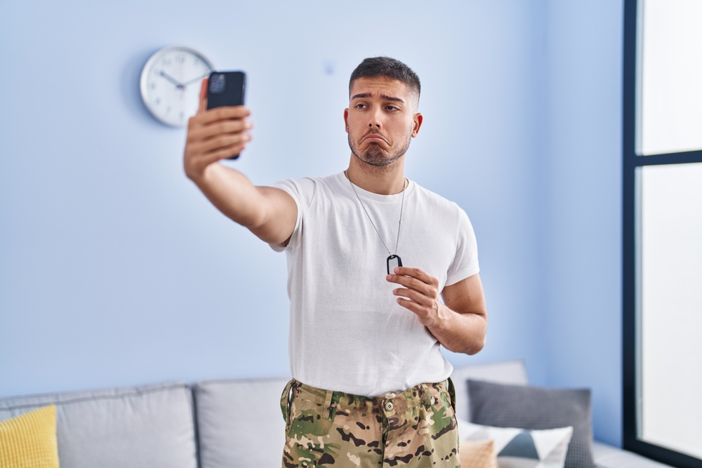 Person looking at smartphone taking a selfie with a concerned expression, representing the impact of social media on self-esteem and mental health